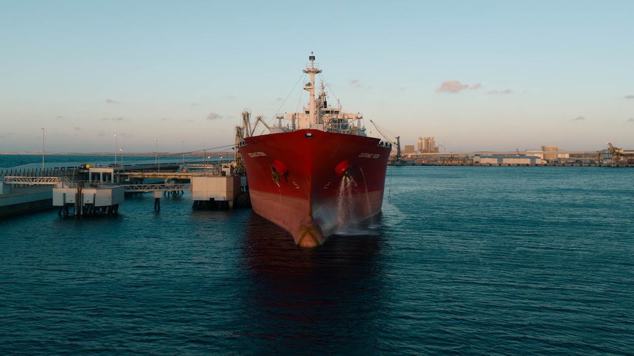 A red cargo ship docked at an industrial port during sunset, capturing maritime trade.