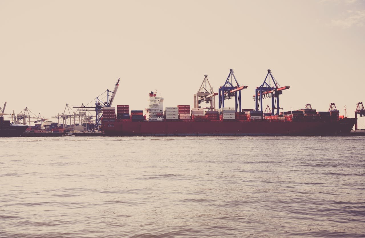 A cargo ship loaded with containers docked at a seaport under clear skies.